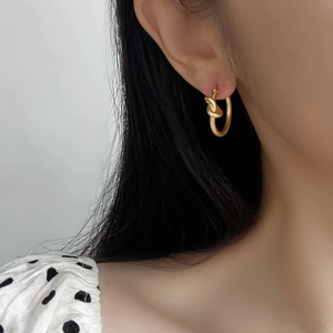 Gros plan de boucles d'oreilles créoles dorées nouées portées par un mannequin de profil