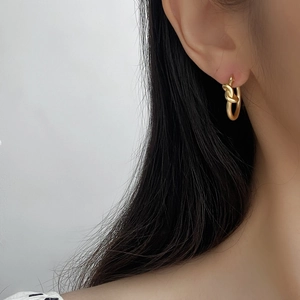 Boucles d'oreilles nœuds dorées mates style minimaliste portées par un mannequin