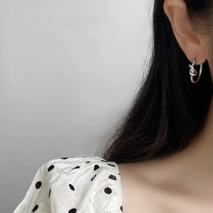 Détail de boucles d'oreilles créoles nouées en argent portées par un mannequin chic