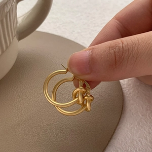 Détail de boucles d'oreilles nœuds dorées montrant le fini mat et le design entrelacé