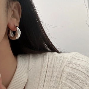 Close-up of thick silver hoop earrings with vertical beaded textures on model