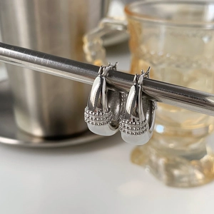 Close-up of silver U-shaped earrings with beaded relief texture on metal stand