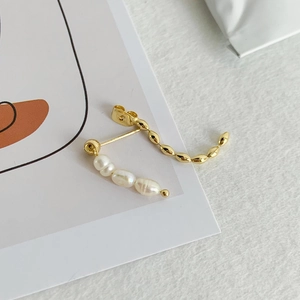 Detail of elegant gold beaded earring with white pearls and asymmetrical curved design