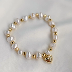 Detailed close-up of Baroque pearl bracelet with golden heart pendant on white silk
