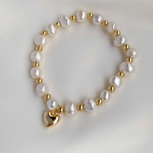 Close-up of white baroque pearls and gold beads with a polished heart pendant on silk