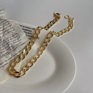 Detailaufnahme einer goldenen Panzerkette mit T-Verschluss auf einem weißen Teller