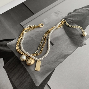 Detail of layered gold bracelet with baroque pearl and engraved heart charm