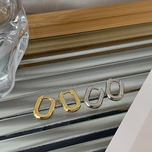 Détail de boucles d'oreilles créoles ovales en or et argent sur un plateau en verre strié