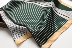 Detail of silk-feel scarf featuring green stripes and grid patterns with yellow borders
