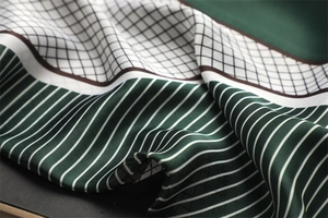 Macro shot of dark green geometric patchwork silk scarf showing soft satin texture and folds