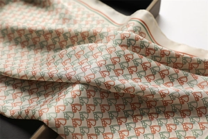 Detailed view of horse-head print silk scarf with elegant orange and green accents