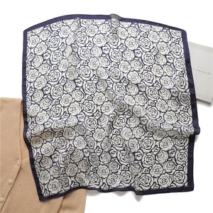 Close-up of navy floral silk scarf with dark blue roses and contrast hem on white background