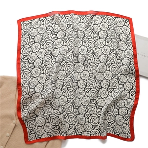 Detail of square silk scarf with camellia pattern and red border on white background