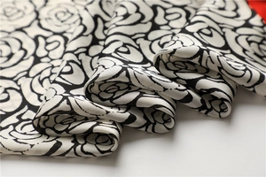 Detailed close-up of white satin scarf with elegant black hand-drawn camellia flowers