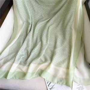 Detailed macro of soft green and cream chain-link pattern scarf on neutral background