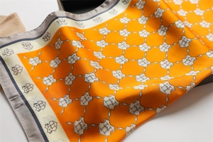 Detail of silk scarf showing smooth texture with orange and grey H-letter pattern