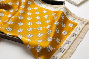 Close-up of elegant yellow silk scarf with H-letter chain pattern and satin texture