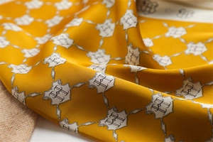 Macro shot of yellow silk scarf featuring elegant H-pattern crests and smooth texture