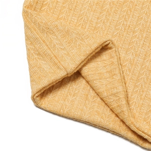Détail macro d'une écharpe en maille jaune moutarde avec motifs ajourés et texture douce