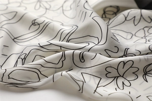 Detail shot of a beige silk scarf showing flowing drapes and minimalist black line art