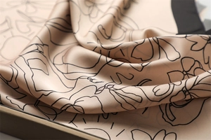 Close-up of champagne silk scarf featuring intricate black floral patterns and glossy texture