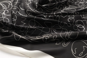 Close-up of elegant black silk scarf with white floral patterns and soft fabric folds