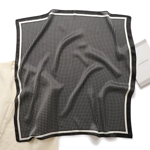 Detail of elegant black and white checkered silk square scarf next to a knit cardigan