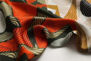 Close-up of geometric silk scarf fabric with orange and green abstract patterns