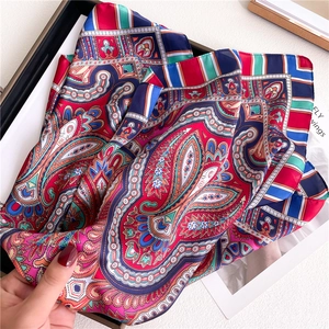 Close-up of bohemian paisley silk scarf showing vivid red and blue patterns with satin sheen