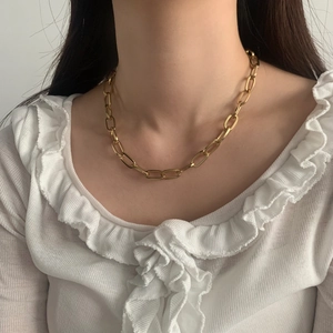 Collana a catena dorata con grandi maglie ovali indossata su una camicetta di pizzo