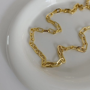 Dettaglio della catena a maglie rettangolari placcate oro disposta su un piatto di ceramica