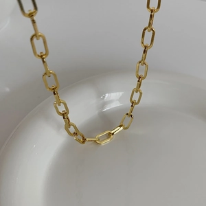Dettaglio di una collana a catena a maglie color oro su ceramica bianca
