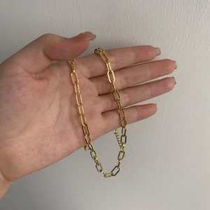 Dettaglio della mano con una collana a catena a graffetta in oro lucido punk