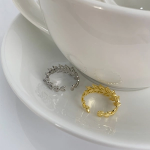 Detail of adjustable leaf rings in gold and silver finish on a white ceramic saucer