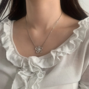 Close-up of a silver floral pendant with zircon inlay worn over a white ruffled collar