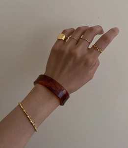 Detail of stacked gold square signet rings paired with a resin amber bangle on model