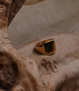 Detailed view of square gold-plated ring with polished mirror finish on rustic wood stand