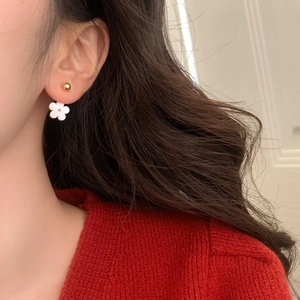 Detail of white five-petal flower earring with golden bead stud on a female model