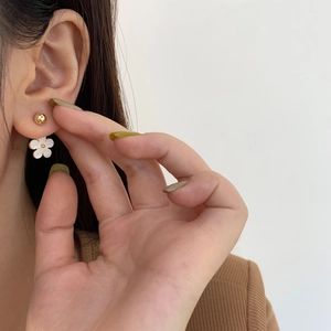 Close-up of elegant white five-petal flower earring with gold bead detail worn by model