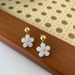 Close-up of small white flower earrings with gold beads on rustic wood background
