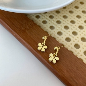 Macro shot of gold five-petal flower earrings with white enamel on a dark wood tray