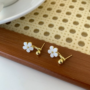 Macro shot of gold plated flower stud earrings with white resin petals on wood background