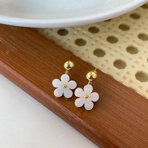 Minimalist gold flower earrings with white petals and pearlescent finish on wooden tray