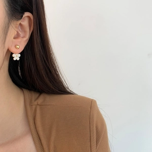 Minimalist gold ball stud earrings with white flower pendants shown on a model's ear
