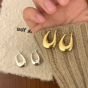 Macro detail of high-polish U-shape earrings in gold and silver finish on soft texture
