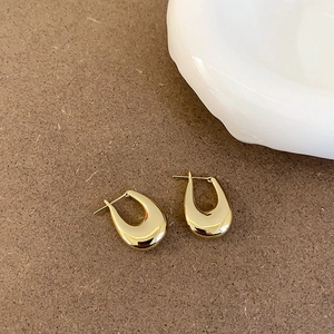 Detailed view of gold-plated U-shaped horseshoe earrings on a minimalist brown background
