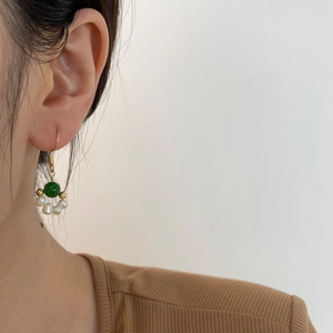 Close-up of elegant gold-plated ear hook with emerald bead and freshwater pearls on model