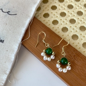 Macro shot of gold-plated hook earrings with emerald green beads and small white pearls