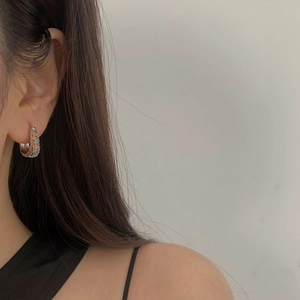 Close-up of small silver hoop earrings with multicolored zircon stones on model's ear