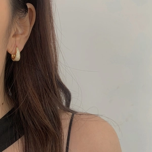 Close-up of a gold U-shaped earring with white cubic zirconia on a model's ear